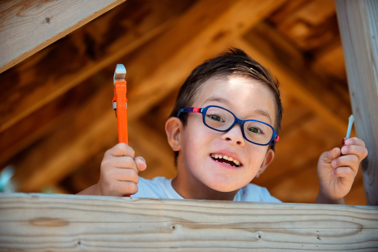 A young boy with glasses holding a paint brush.